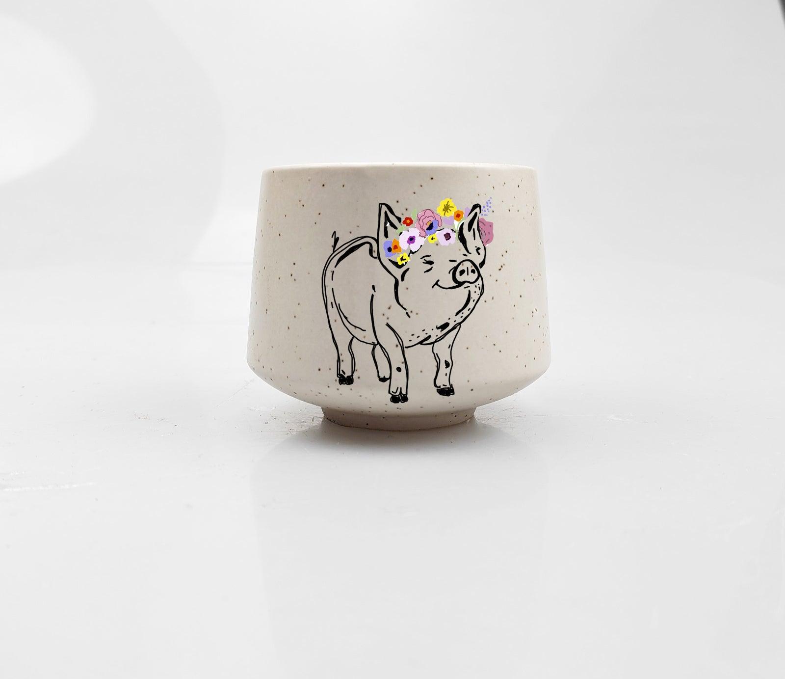 Artsy Ems Designs presents the Artisan Piglet Cup—a charming white ceramic cup featuring a smiling pig with a colorful flower crown, perfect as whimsical home decor.
