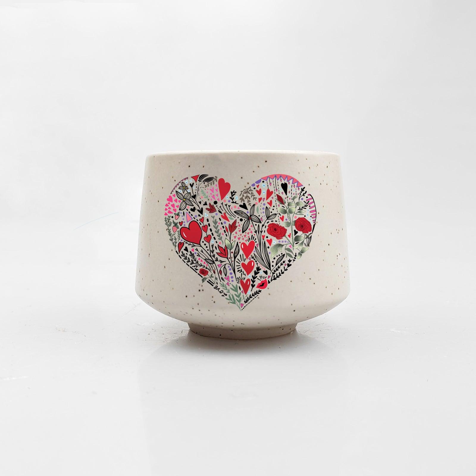 Artsy Ems Designs Heart Explosion Mini Cup is a white, durable ceramic cup with a speckled finish, featuring a large heart-shaped floral design in red, pink, and green on the front and a slightly rounded shape.